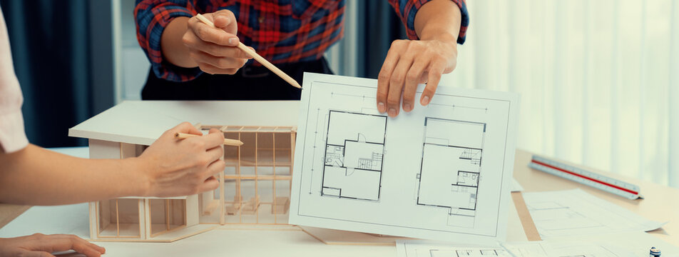 Cropped image professional architect hand compare construction between blueprint and house model while coworker pointing the difference point. Creative and teamwork concept. Closeup. Burgeoning.