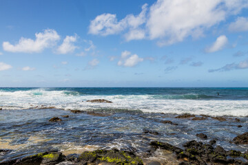 Fototapeta na wymiar a beautiful spring landscape at Sandy Beach with blue ocean water, silky brown sand, rocks covered in green algae, crashing waves, blue sky and clouds in Honolulu Hawaii USA