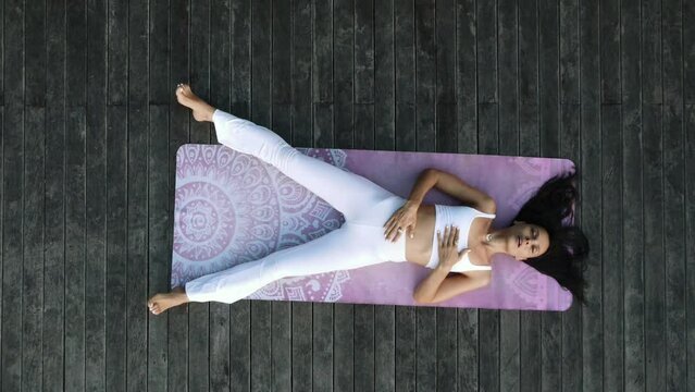 A beautiful young girl of European appearance, brunette, doing yoga, doing breathing exercises, in a stylish white yoga suit.