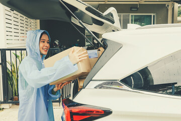 Asian businesswoman driving delivery running business online ordering wholesale retail online logistics wearing raincoat delivering parcel boxes in the rainy season to customers in front of the house.