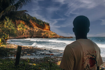 A photo of a man staring off into the distance at the beach marveling at the sight before him which was taken from the back
