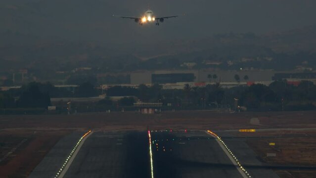 The airplane lands on the lighted runway of the airport at dusk