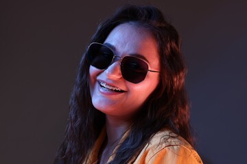 Portrait of beautiful young woman with stylish sunglasses on color background with neon lights