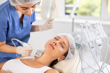 Young adult female patient experiencing cryotherapy procedure on neck using ice hammer to tighten...