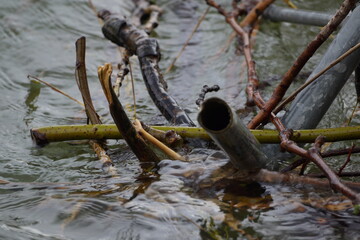 Macro of clutter of metal pipes and branches stuck in a river