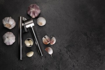 Garlic press, bulbs and cloves on grey table, flat lay. Space for text