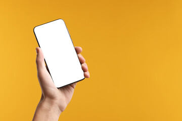 Man holding smartphone with blank screen on yellow background, closeup. Mockup for design