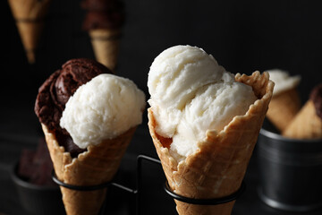 Ice cream scoops in wafer cones on stand against dark background, closeup