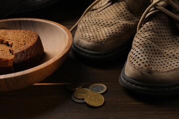 Poverty. Old shoes, pieces of bread and coins on wooden table, closeup - obrazy, fototapety, plakaty