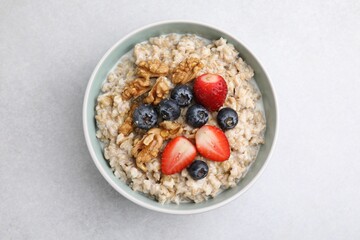 Tasty oatmeal with strawberries, blueberries and walnuts in bowl on grey table, top view