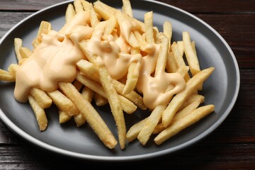 Delicious french fries with cheese sauce on wooden table, closeup