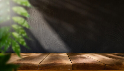Empty natural wooden table next to a black wall, dark tones, with plant leaves outdoors. Brown...