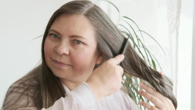 comb, brush in female hand, woman combing long brown hair, tangles of fallen hair wound on brush pins, concept hair loss, health, causes, symptoms and treatment alopecia, hormonal imbalance