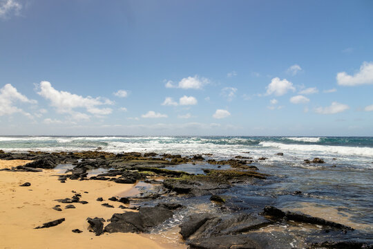 a beautiful spring landscape at Sandy Beach with blue ocean water, silky brown sand, rocks covered in green algae, crashing waves, blue sky and clouds in Honolulu Hawaii USA