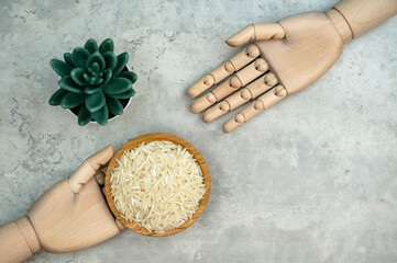 A wooden bowl of rice grains is held by mannequin hand (with decoration of another mannequin hand),...