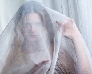 Portrait of a young woman covered with white mesh fabric. A woman hides her face behind a veil cloth. - 775509764
