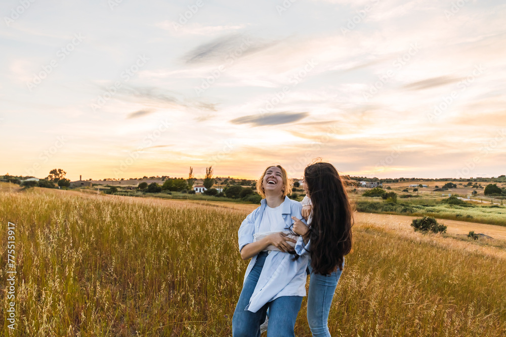 Wall mural two young women laughing and having fun in a field at sunset