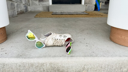 Child's shoes and sunglasses sitting on a front porch