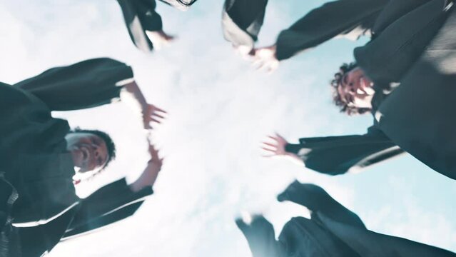 People, students and hands together with celebration for graduation, teamwork or support below blue sky. Low angle or group of graduates piling in success for education, unity or solidarity in nature