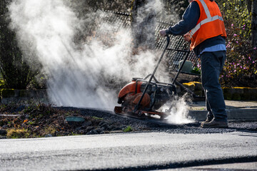 Construction worker using a plate compactor to finish the fresh asphalt at the end of a sidewalk...
