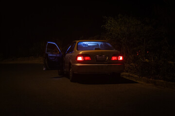 Carro sedan plomo antiguo vacío en una autopista con la puerta abierta y las luces prendidas roja...