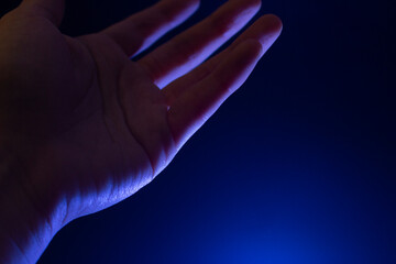 Palma de una mano mirando hacia arriba alzada sobre un fondo azul iluminado con una luz blanca que...