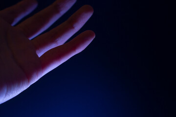 Palma de una mano mirando hacia arriba alzada sobre un fondo azul iluminado con una luz blanca que...