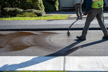 Construction worker spraying asphalt binder as a primer for the next layer of blacktop in a road...