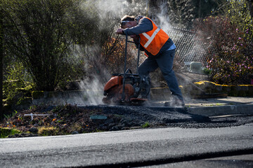 Construction worker using a plate compactor to finish the fresh asphalt at the end of a sidewalk while early morning sun highlights the steam and smoke, road re-paving project
 - obrazy, fototapety, plakaty