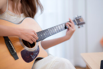 Closeup hands of young asian woman sitting on sofa playing guitar in living room at home, skill and...