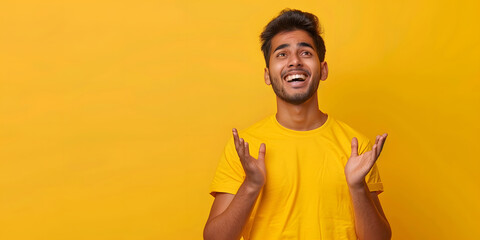 Emotion of joy, celebration of victory. Handsome Indian man is sincerely happy, looking to the side and making a winning gesture while standing against a yellow background. Copy space