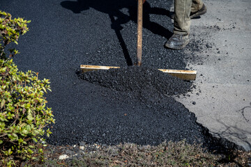 Construction worker with asphalt rake smoothing out fresh blacktop on driveway
