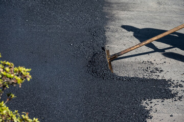 Construction worker with asphalt rake smoothing out fresh blacktop on driveway
 - obrazy, fototapety, plakaty