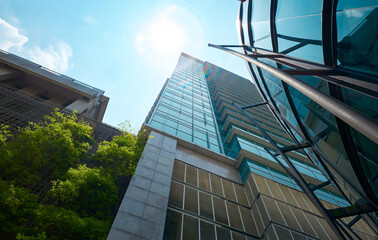 Low angle view of modern glass buildings and green with bright sky