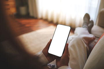 Mockup image of a woman holding mobile phone with blank desktop white screen while sitting on a sofa at home - 775550309
