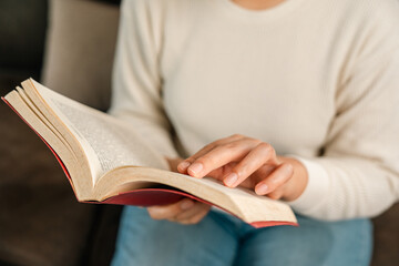 Asian woman sitting reading book on cozey couch sofa in living room with sun light morning. People stay home part time relax at home. Good time quality life rest calm happiness