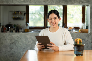 Young asian beautiful business woman working with tablet sitting at home. Smiling charming happy young female doing homework meeting conference with team at home.