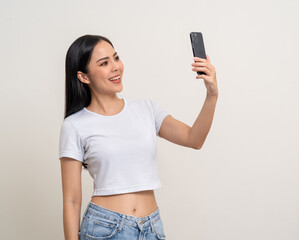 Happy Beautiful young asian woman using smartphone mobile to selfie take photo herself standing on isolated white background. Attractive female with cell phone capture the frame