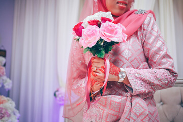 Close up of bride's hand with henna painted wearing wedding ring holding a rose bouquet in traditional Islamic wedding. Selective focus.