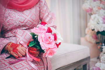 Close up of bride's hand with henna painted wearing wedding ring holding a rose bouquet in traditional Islamic wedding. Selective focus.