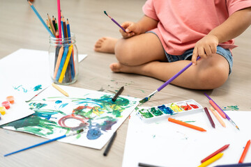 Happy moment little cute girl creating and water color painting activity with paint brushes on frame canvas at living room. Kids activity. Child physical, Emotional, Cognitive development concept.