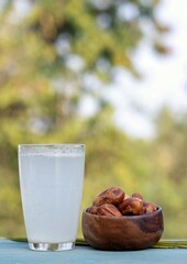 Khejur Rosh or Date Palm Tree Juice in Glass with Phoenix Dactylifera Fruit in a Wooden Bowl Isolated on Wooden Table Background with Copy Space, Also Known as Date Palm Sap or Khejur Ras
