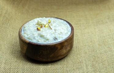 Cracked Wheat Kheer or Payesh Garnished with Cashew, Almond, Pistachio in a Wooden Bowl Isolated on Bulap Fabric Background with Copy Space, Also Known as Ksheeram, Milk Pudding