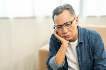 Asian mature old man sitting bored serious thinking in living room at home. Portrait of serious...