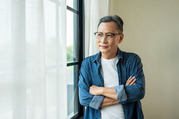Handsome asian mature old man standing near windows with sunlight in the morning. Happy Portrait of cheerful smiling senior asian man pose looking at camera. Mature People and lifestyle