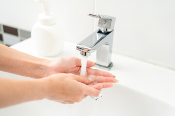 Woman hands are turning on the faucet at home and washing hands with clean water and soap for good...
