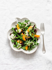 Delicious salad with beetroot, arugula, cheese and oranges on a light background, top view