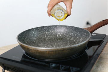Woman hand pouring cooking oil from bottle into frying pan on stove