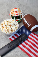 Remote control, popcorn, helmet, rugby ball and American flag on grey background. Superbowl concept