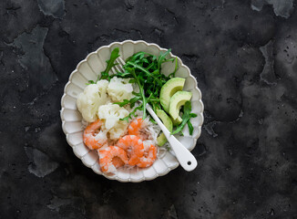 Lunch diet - rice, shrimp, boiled cauliflower, arugula, avocado in one plate on a dark background, top view